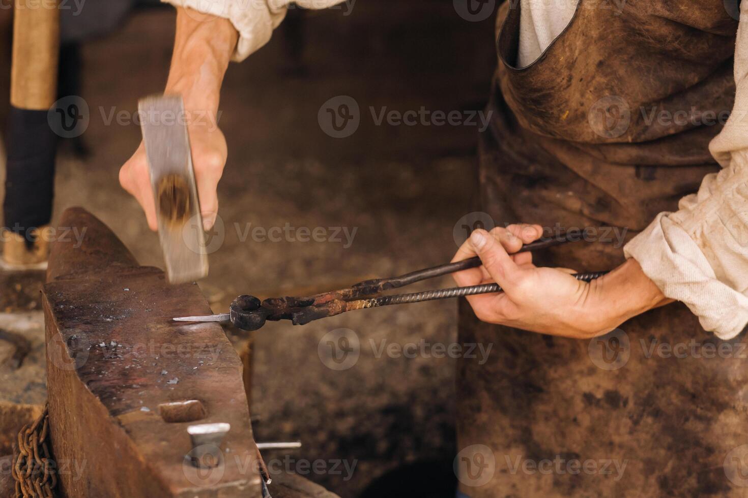 A blacksmith manually forges red-hot metal on an anvil with a hammer photo