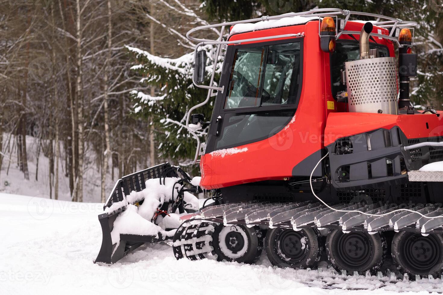 A snowplow on red tracks standing in winter in the forest near the barn photo