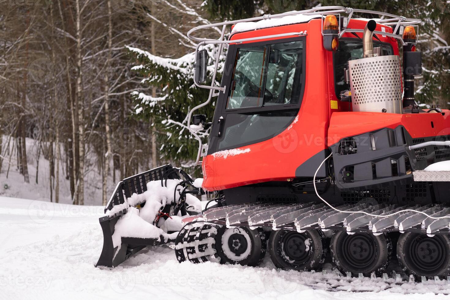 A snowplow on red tracks standing in winter in the forest near the barn photo