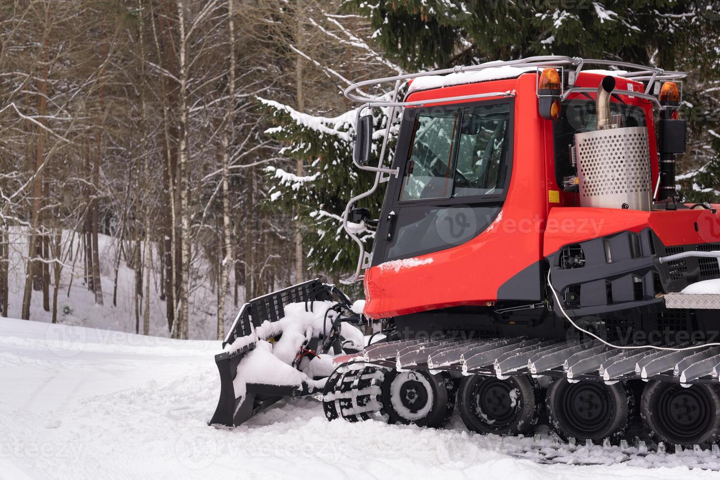 A snowplow on red tracks standing in winter in the forest near the barn photo