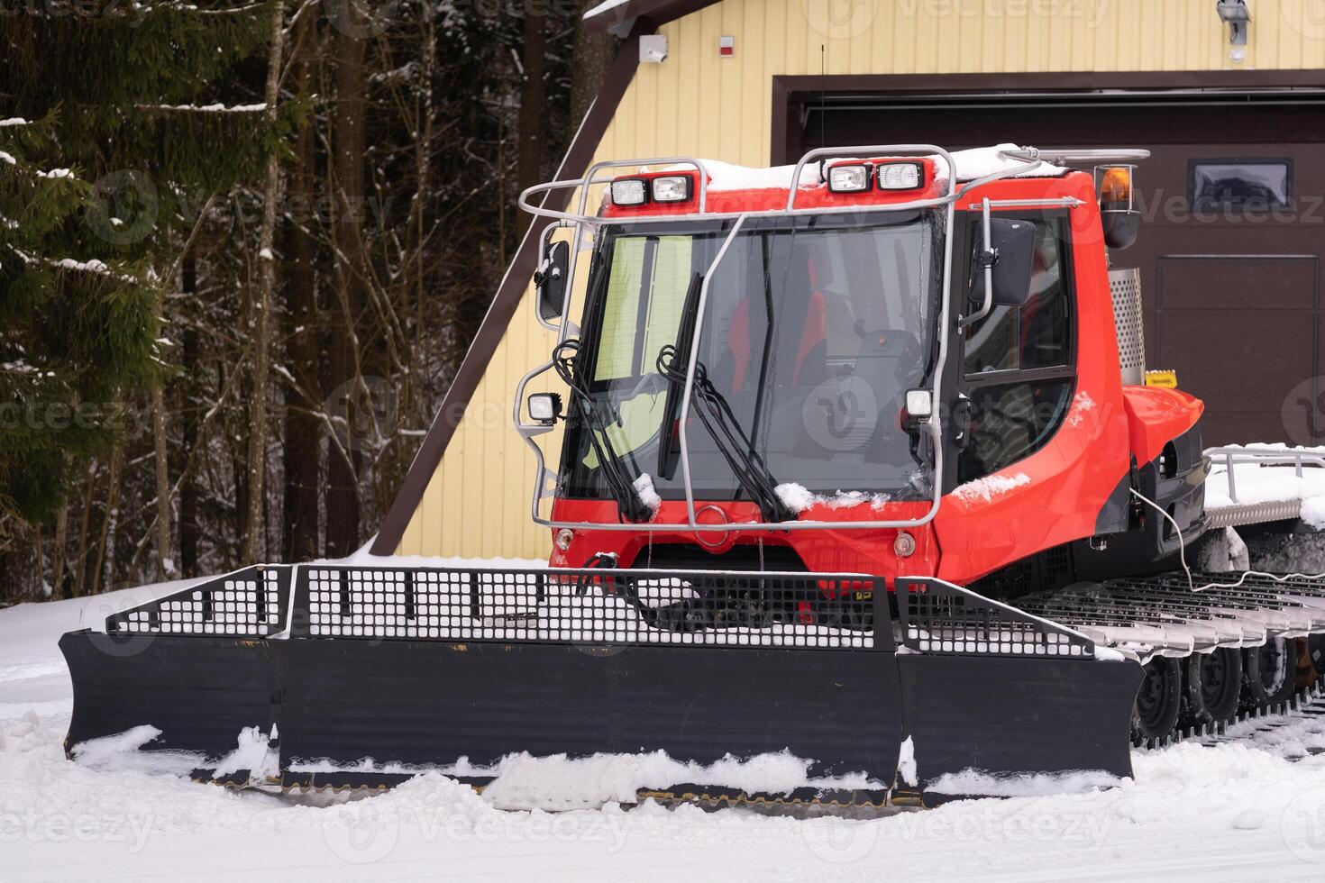 A snowplow on red tracks standing in winter in the forest near the barn photo