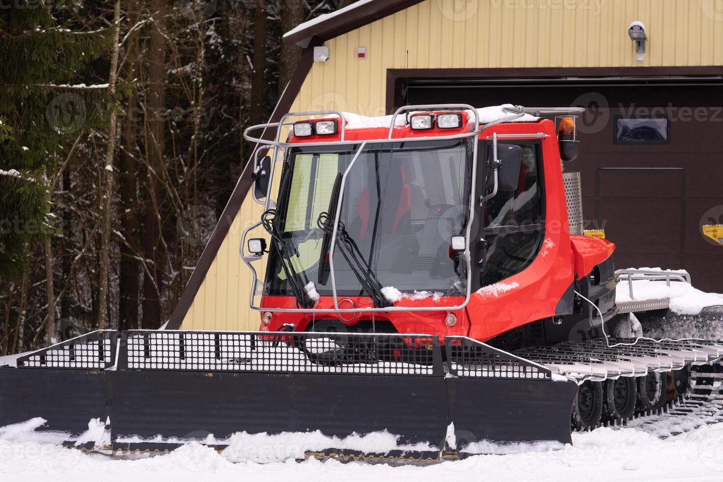 A snowplow on red tracks standing in winter in the forest near the barn photo