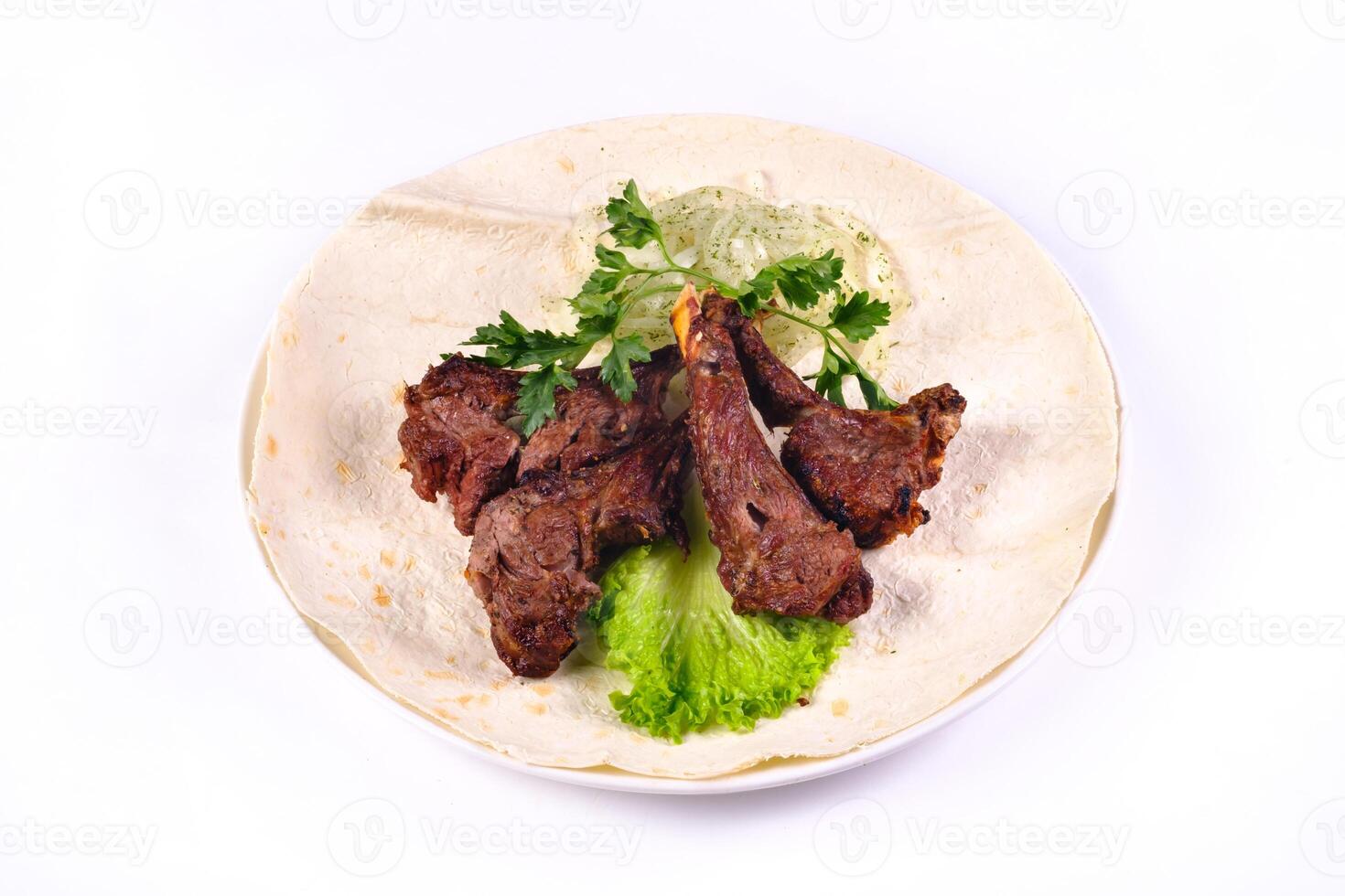Meat kebab on ribs on lavash with onions and cabbage on a white plate, on an isolated white background photo