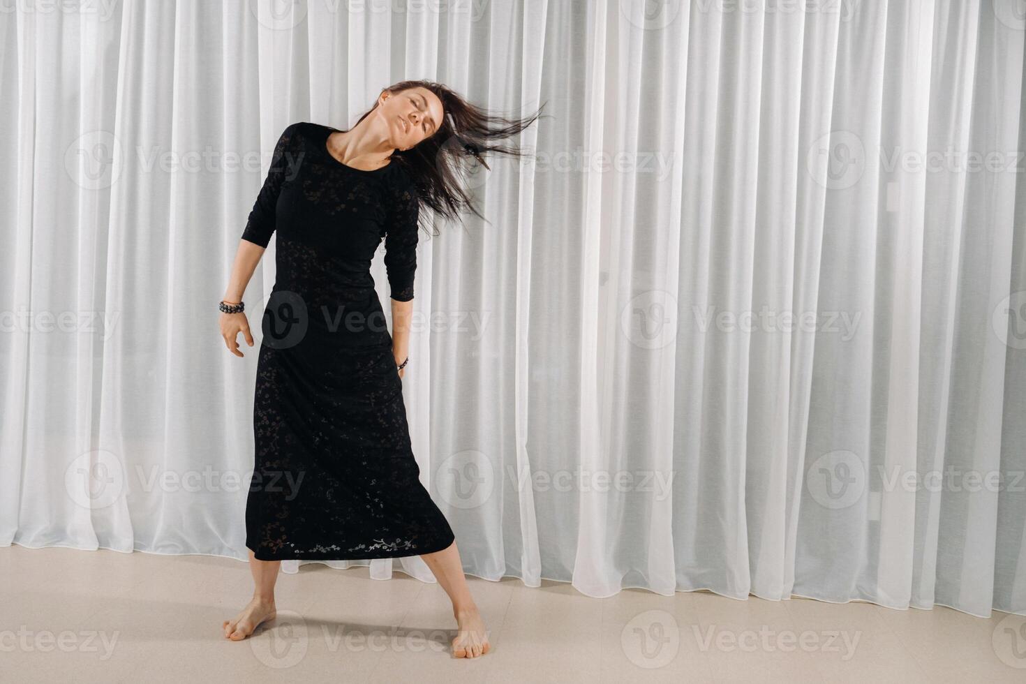 A girl in a black dress moves in a dance on a gray background. Dynamic dance photo