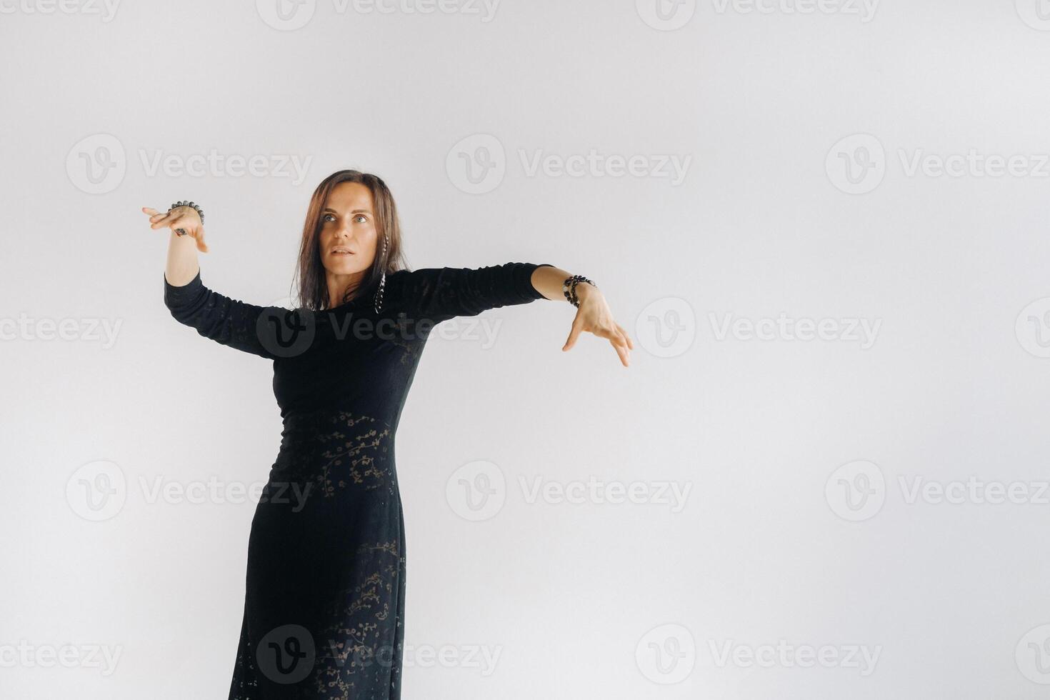A girl in a black dress moves in a dance on a gray background. Dynamic dance photo