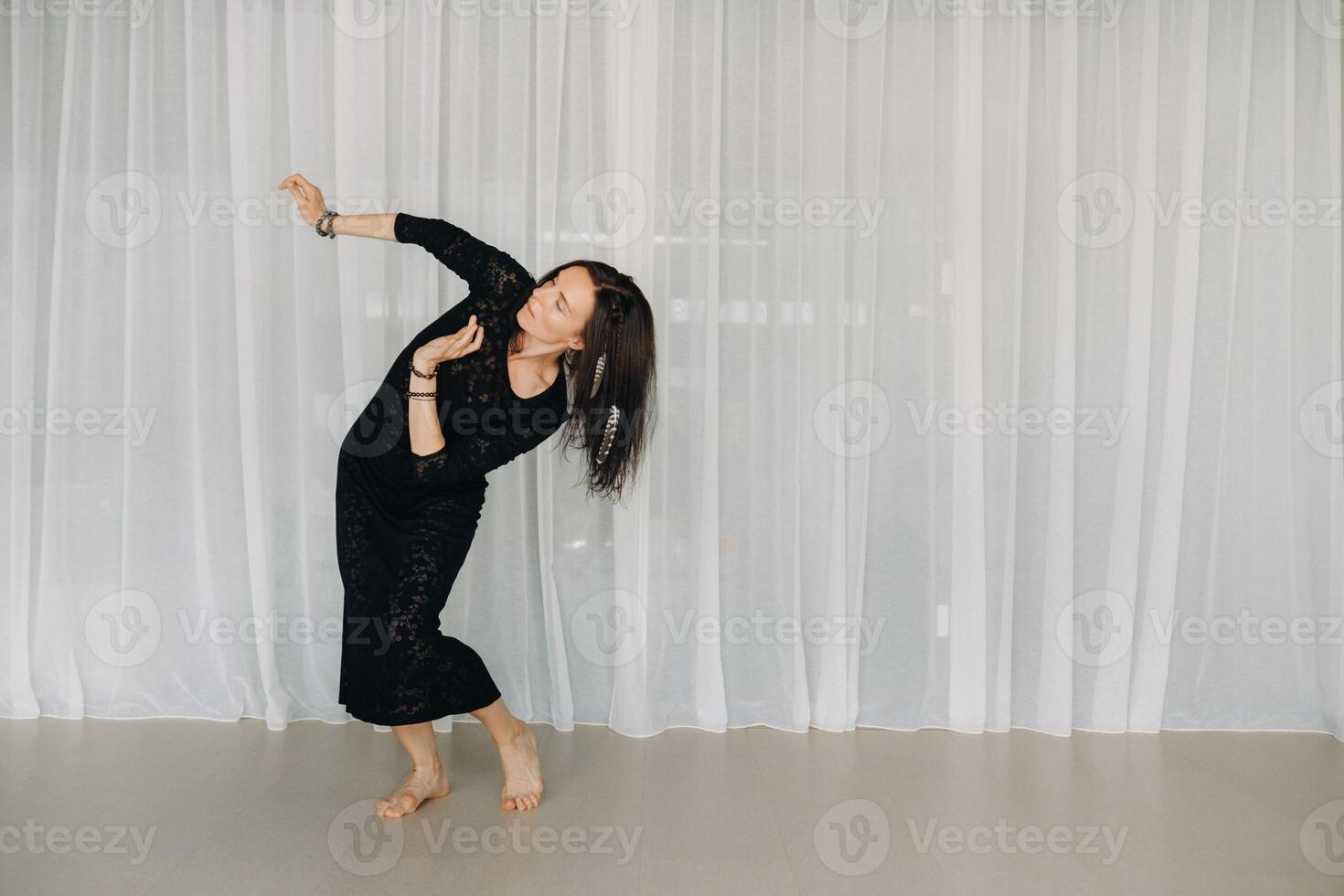 A girl in a black dress moves in a dance on a gray background. Dynamic dance photo