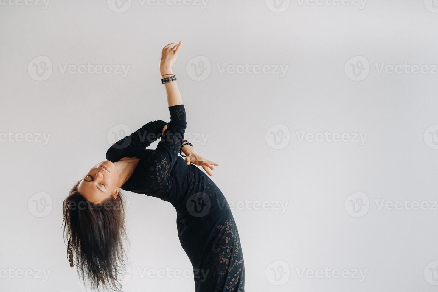 A girl in a black dress moves in a dance on a gray background. Dynamic dance photo