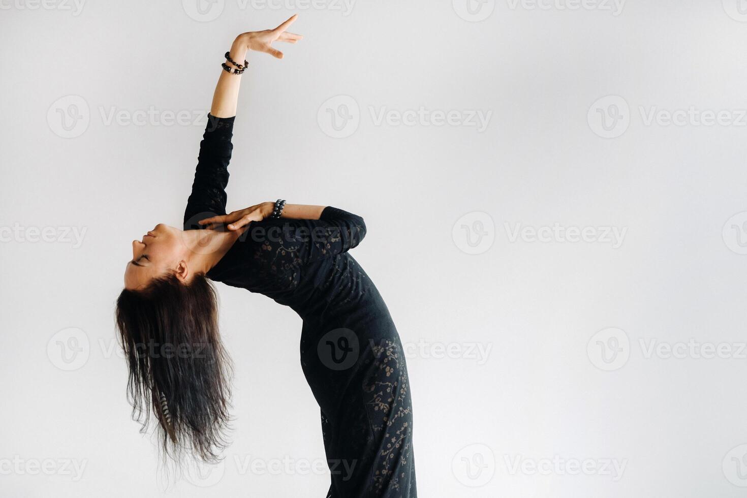 A girl in a black dress moves in a dance on a gray background. Dynamic dance photo