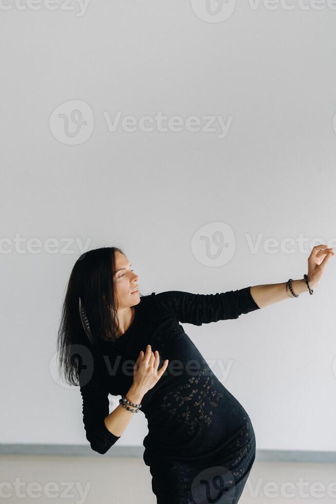 A girl in a black dress moves in a dance on a gray background. Dynamic dance photo