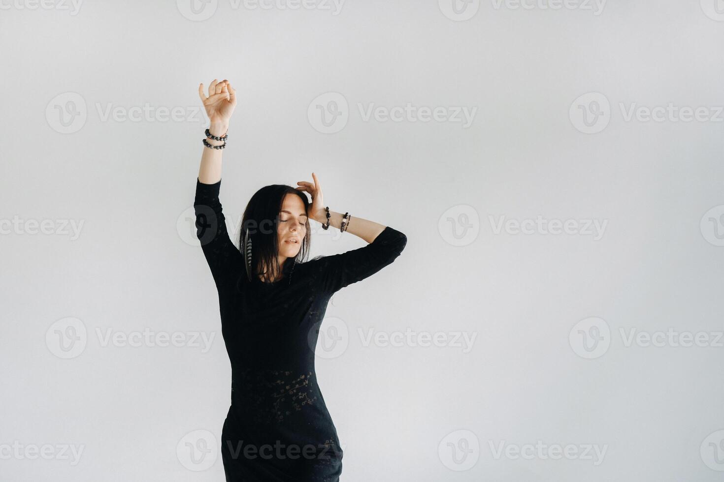 A girl in a black dress moves in a dance on a gray background. Dynamic dance photo