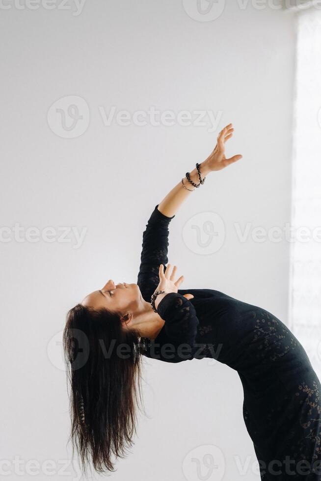 A girl in a black dress moves in a dance on a gray background. Dynamic dance photo
