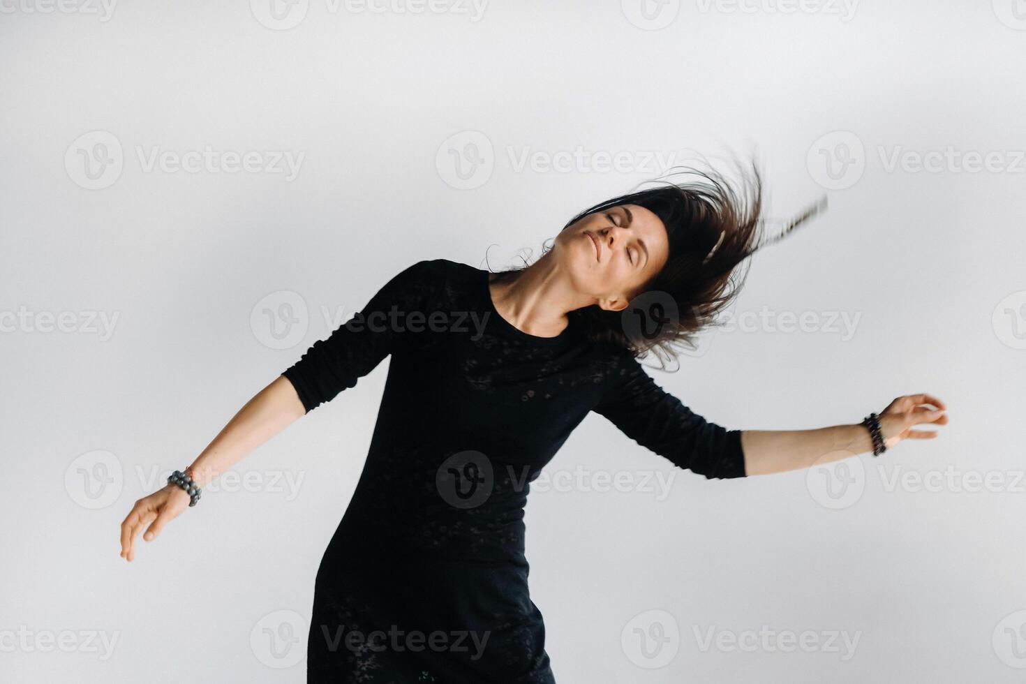 A girl in a black dress moves in a dance on a gray background. Dynamic dance photo