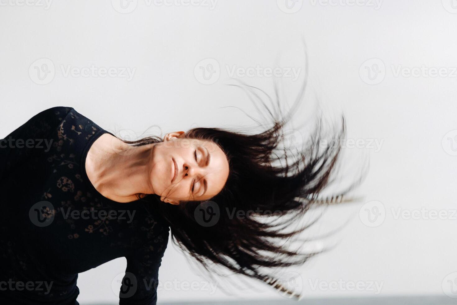 A girl in a black dress moves in a dance on a gray background. Dynamic dance photo