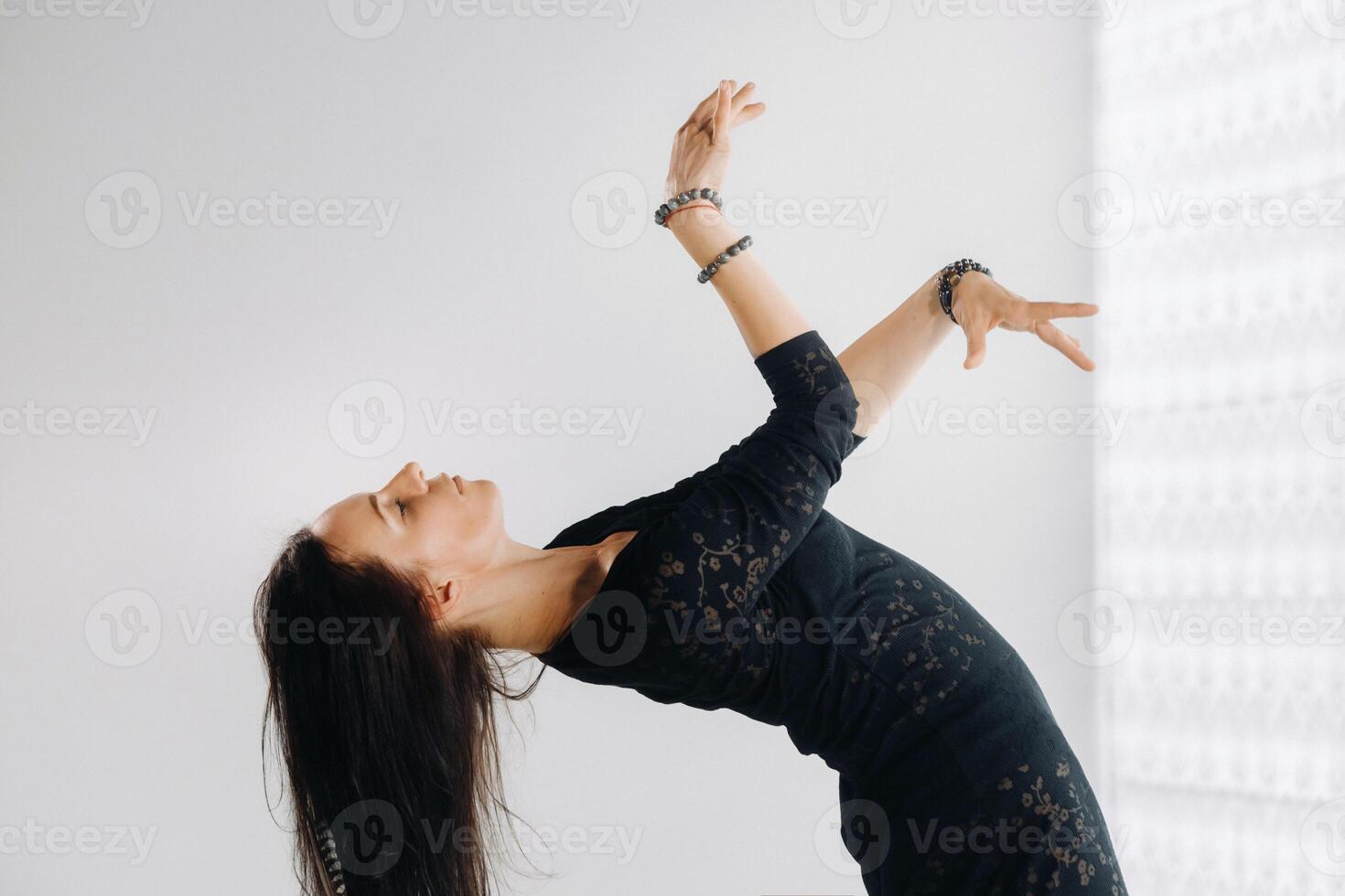 A girl in a black dress moves in a dance on a gray background. Dynamic dance photo