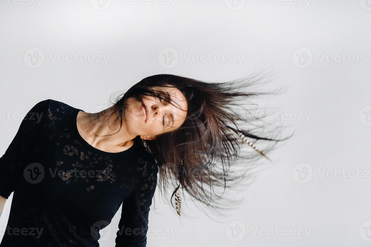 A girl in a black dress moves in a dance on a gray background. Dynamic dance photo