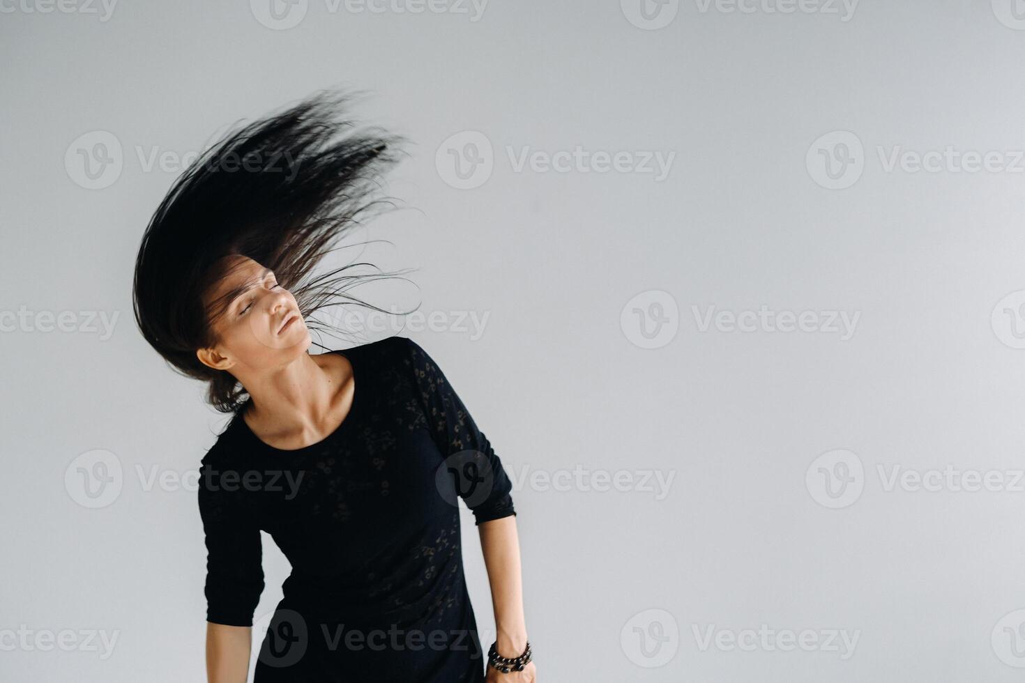A girl in a black dress moves in a dance on a gray background. Dynamic dance photo