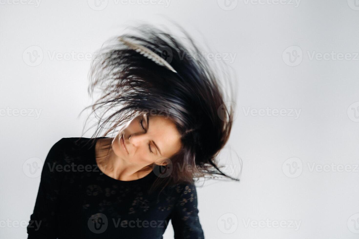 A girl in a black dress moves in a dance on a gray background. Dynamic dance photo
