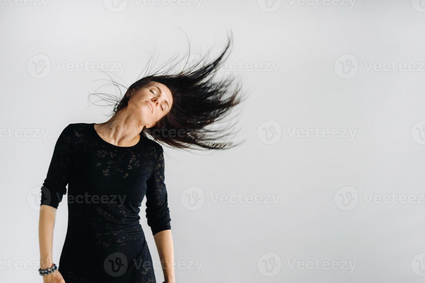 A girl in a black dress moves in a dance on a gray background. Dynamic dance photo