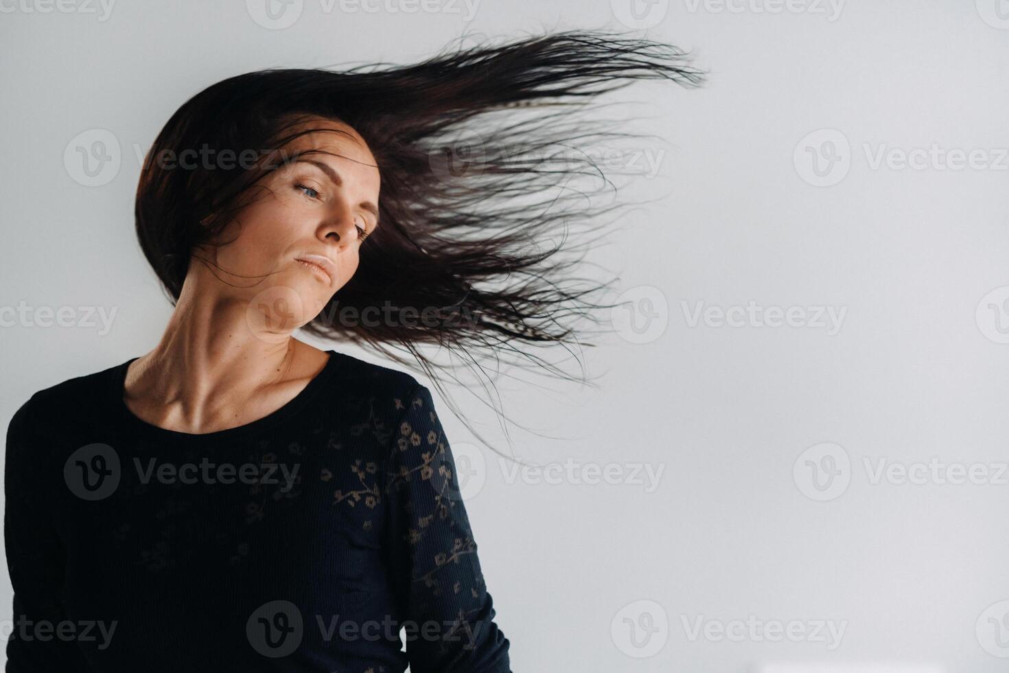 A girl in a black dress moves in a dance on a gray background. Dynamic dance photo