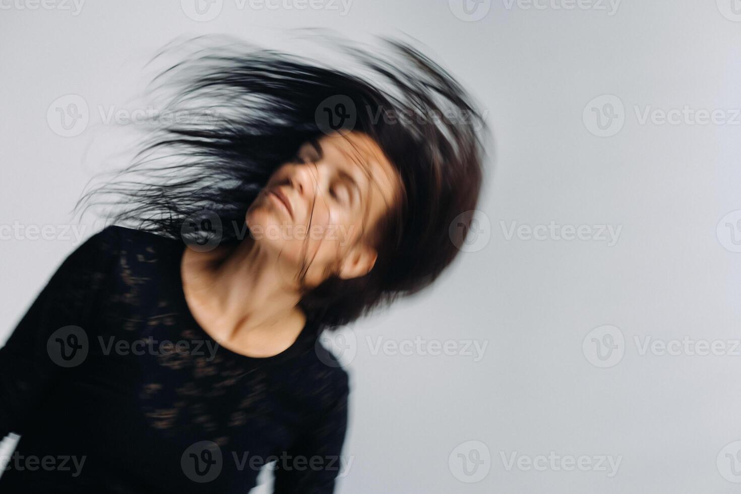 A girl in a black dress moves in a dance on a gray background. Dynamic dance photo
