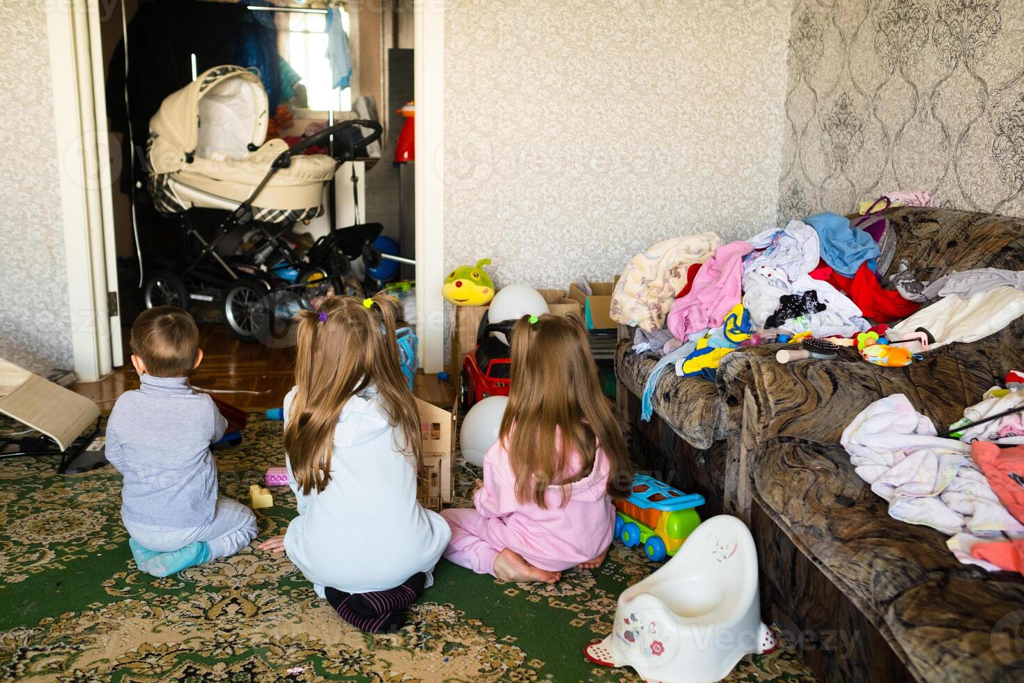 Three unrecognizable children are playing in a dirty cluttered room photo