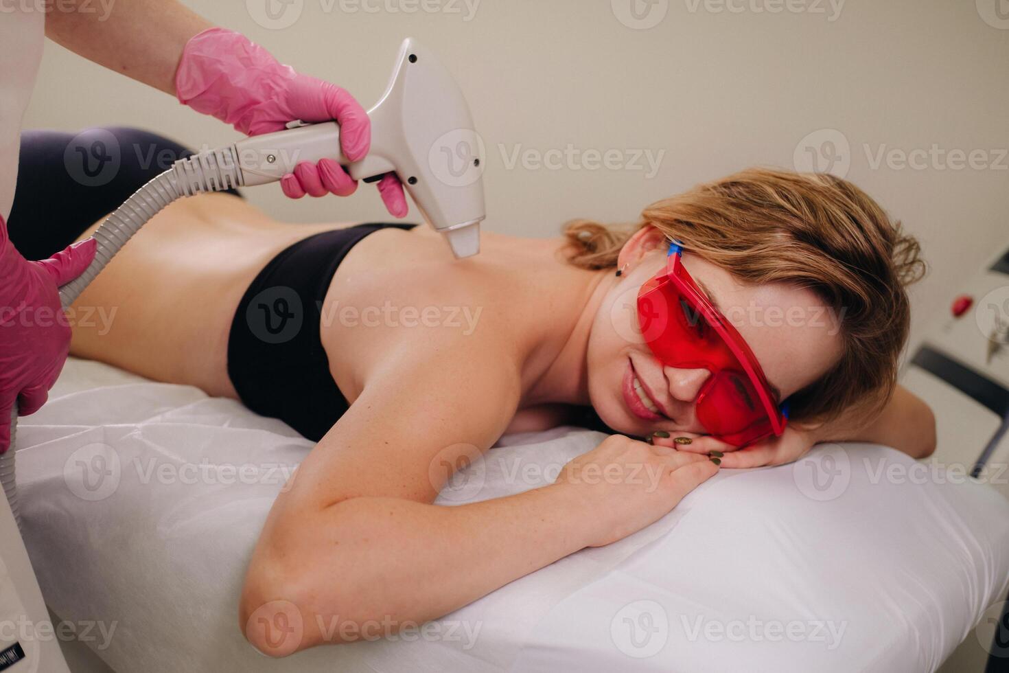 A girl in black underwear does laser hair removal on her back in the salon photo