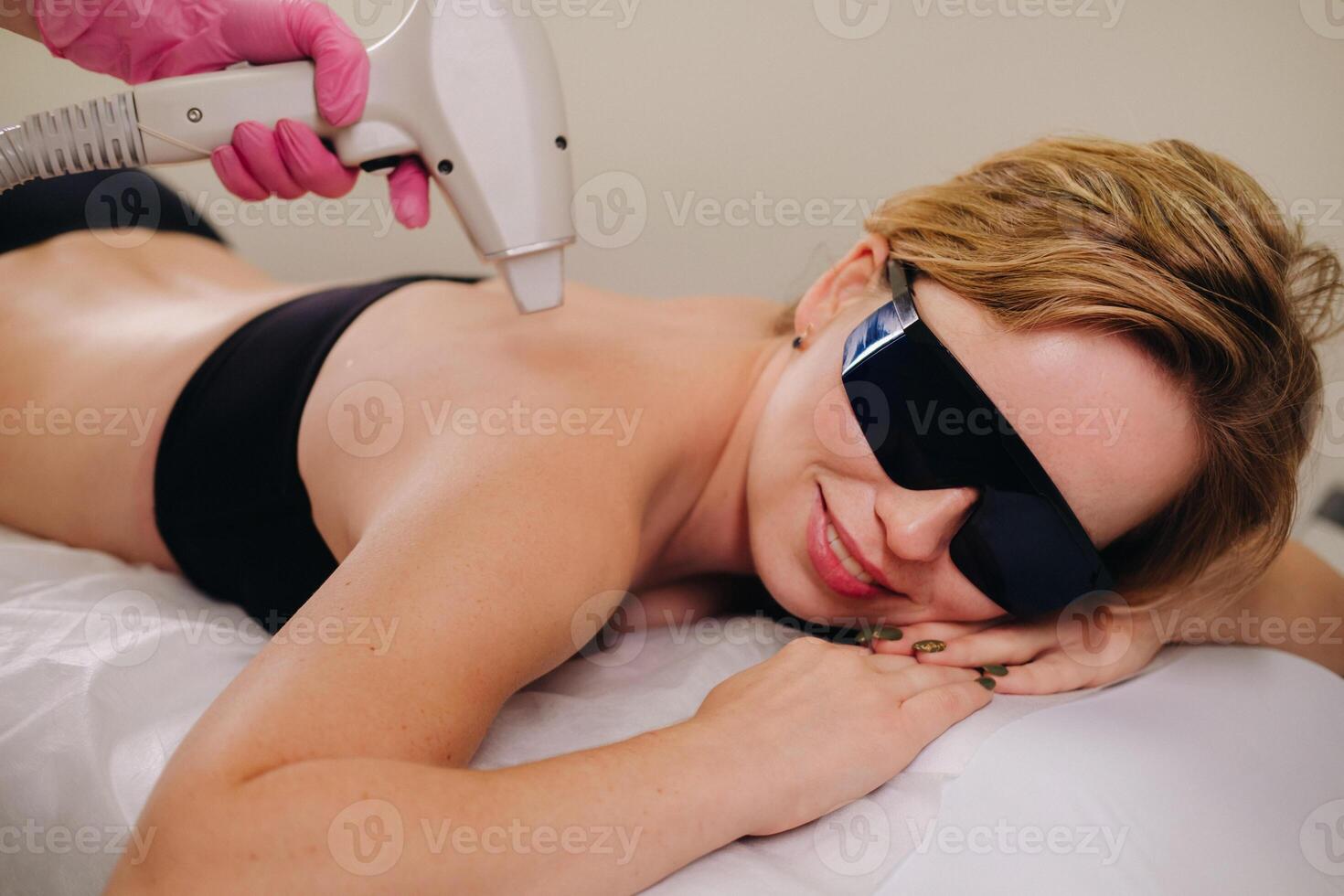 A girl in black underwear does laser hair removal on her back in the salon photo