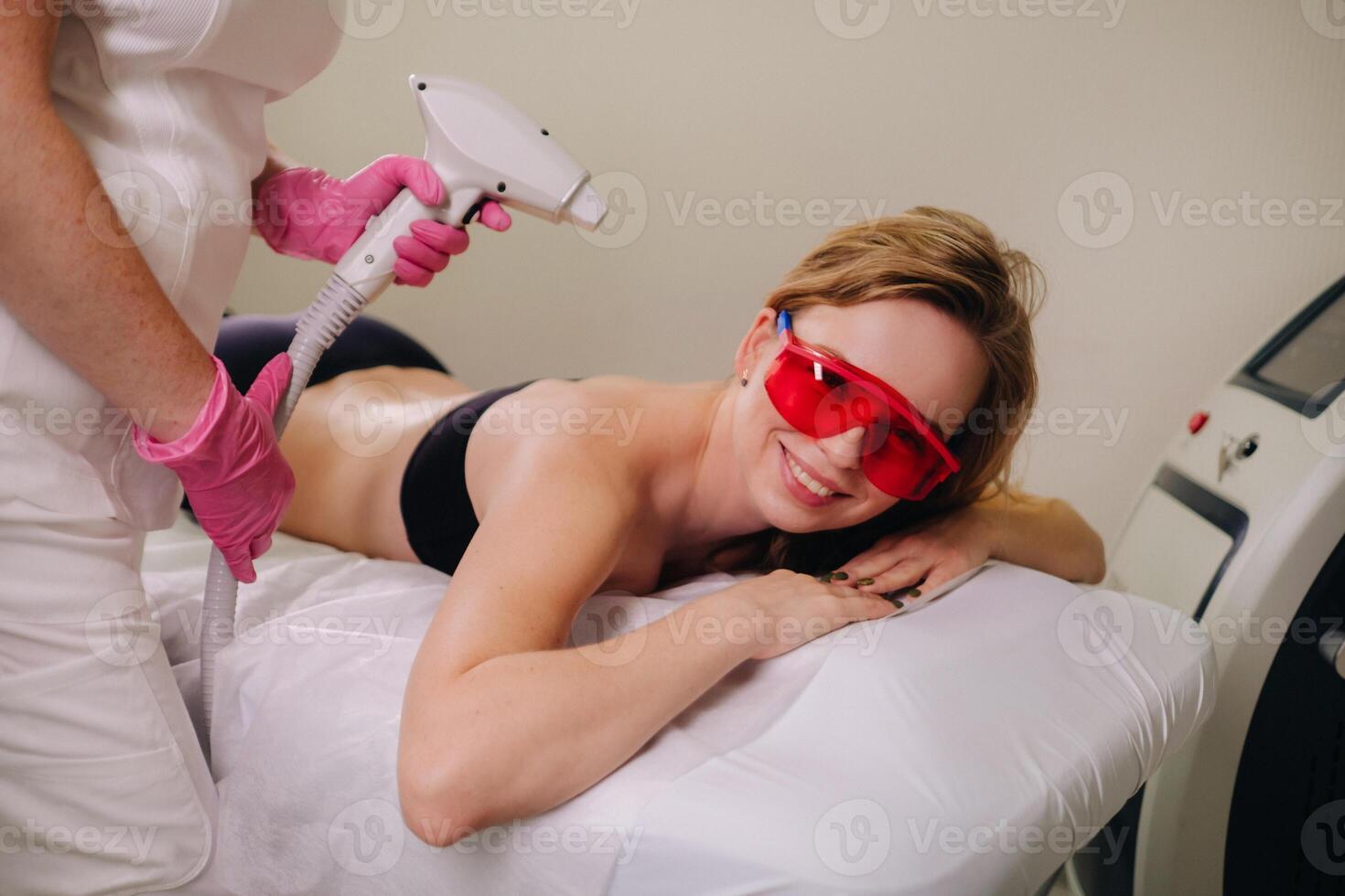 A girl in black underwear does laser hair removal on her back in the salon photo
