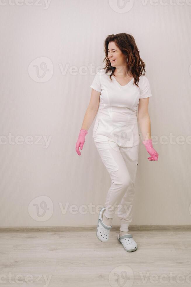 A smiling doctor in pink gloves and a white coat looks at the camera on a light background photo