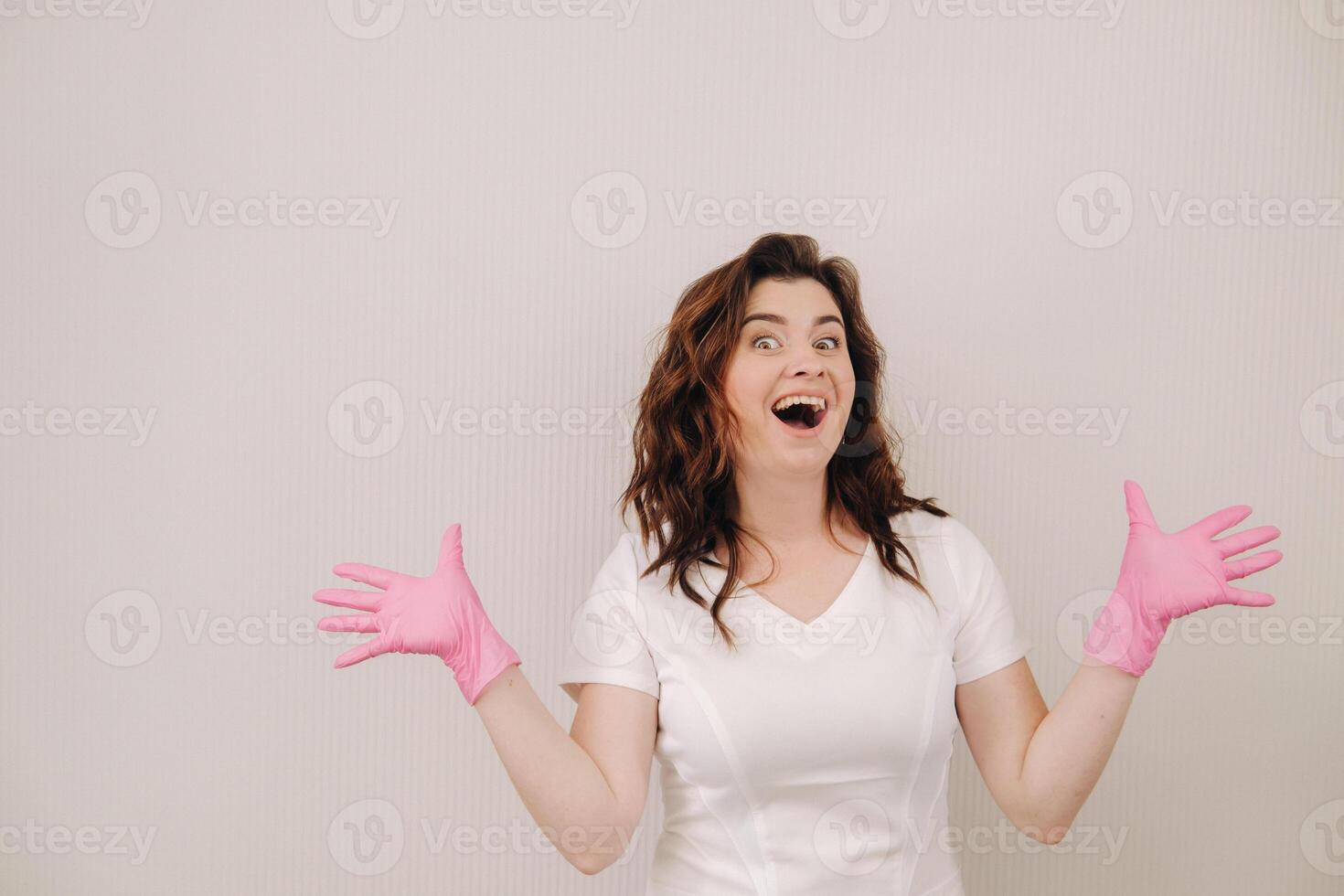 A smiling doctor in pink gloves and a white coat looks at the camera on a light background photo