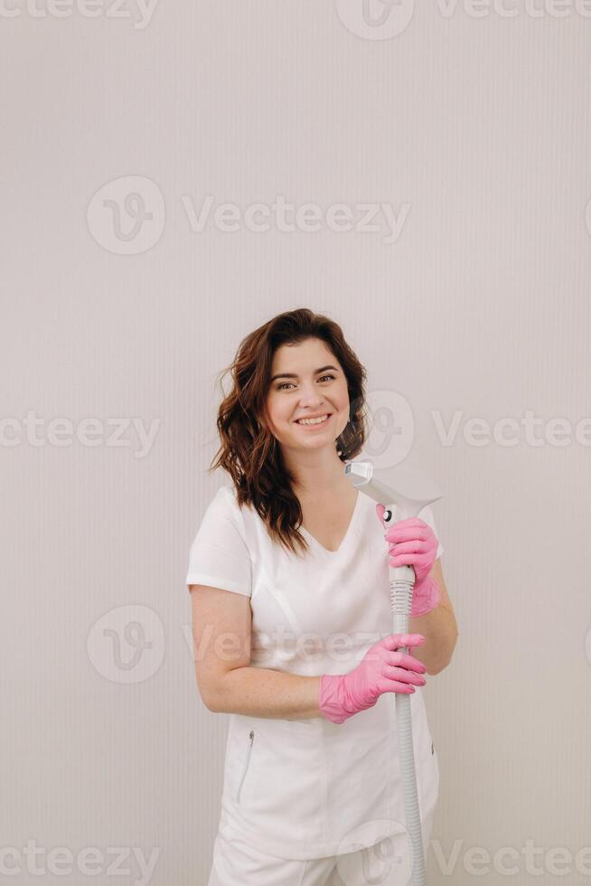 Portrait of the master of laser hair removal. A woman in a white coat holds a laser hair removal device in her hands photo
