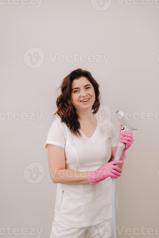 Portrait of the master of laser hair removal. A woman in a white coat holds a laser hair removal device in her hands photo