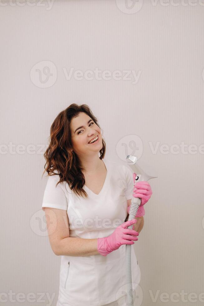 Portrait of the master of laser hair removal. A woman in a white coat holds a laser hair removal device in her hands photo