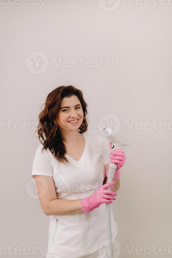 Portrait of the master of laser hair removal. A woman in a white coat holds a laser hair removal device in her hands photo