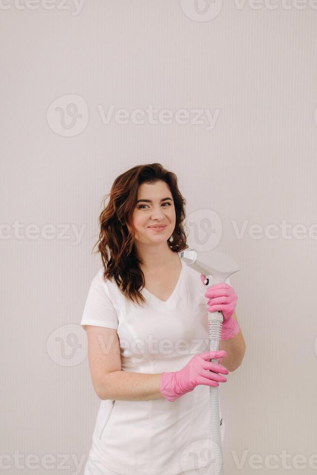Portrait of the master of laser hair removal. A woman in a white coat holds a laser hair removal device in her hands photo
