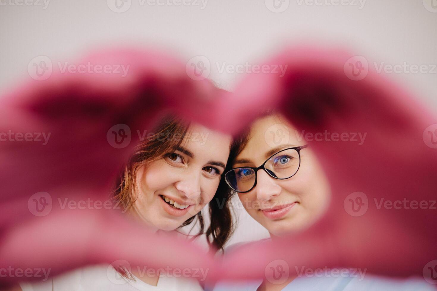 Portrait of two qualified cosmetologists-women, confidently smiling and making a heart with their hands in a medical center photo