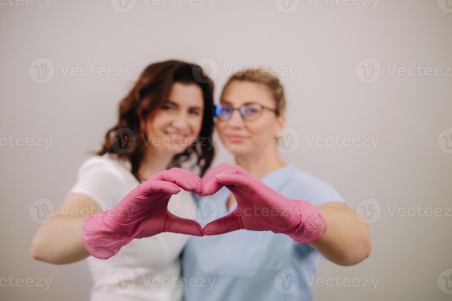 Portrait of two qualified cosmetologists-women, confidently smiling and making a heart with their hands in a medical center photo
