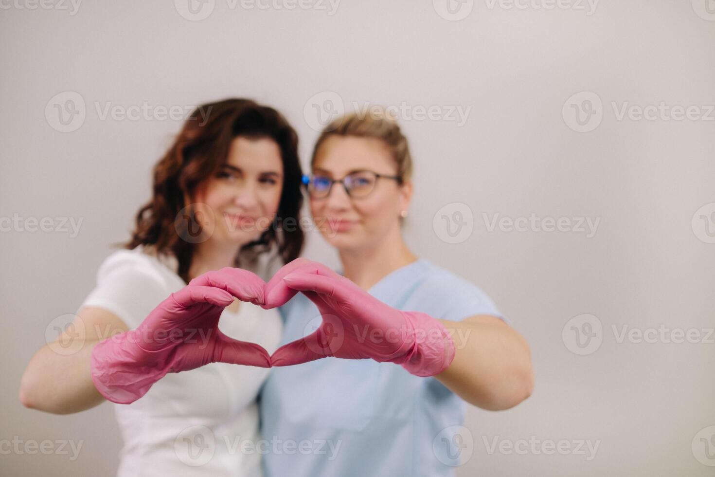 Portrait of two qualified cosmetologists-women, confidently smiling and making a heart with their hands in a medical center photo