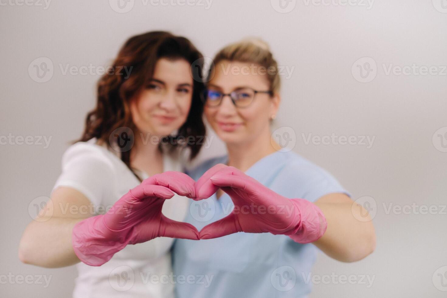 Portrait of two qualified cosmetologists-women, confidently smiling and making a heart with their hands in a medical center photo