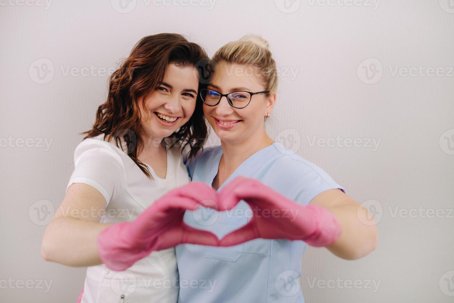 Portrait of two qualified cosmetologists-women, confidently smiling and making a heart with their hands in a medical center photo