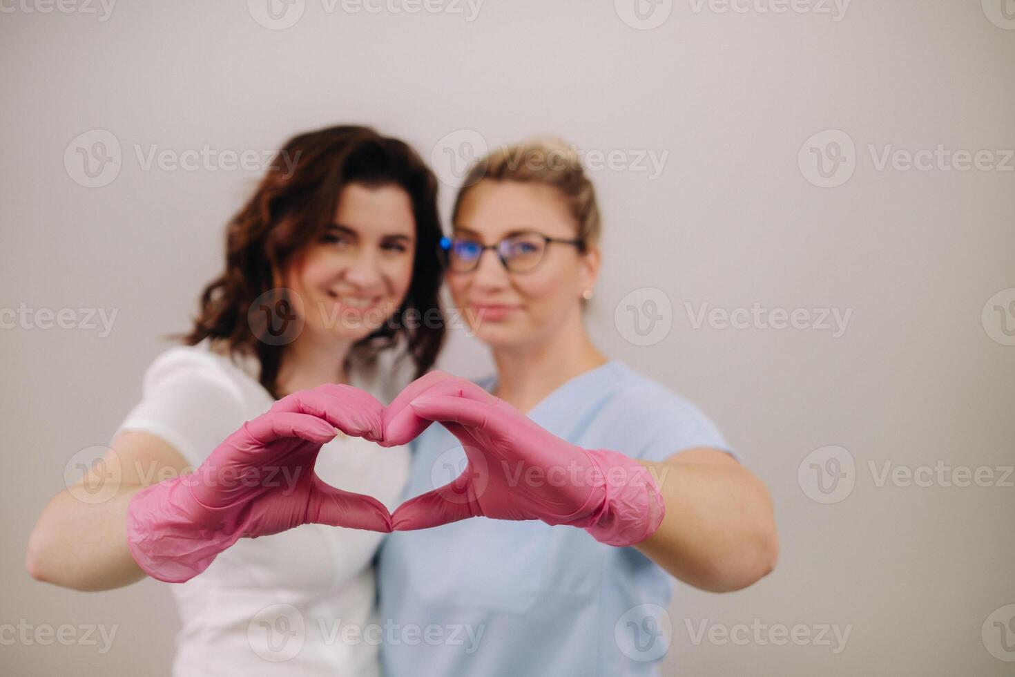 Portrait of two qualified cosmetologists-women, confidently smiling and making a heart with their hands in a medical center photo