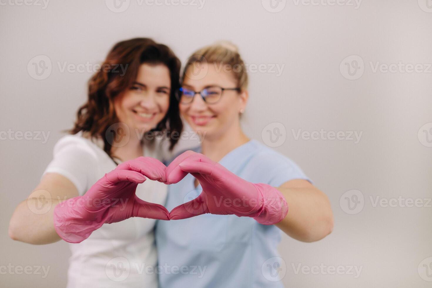 Portrait of two qualified cosmetologists-women, confidently smiling and making a heart with their hands in a medical center photo
