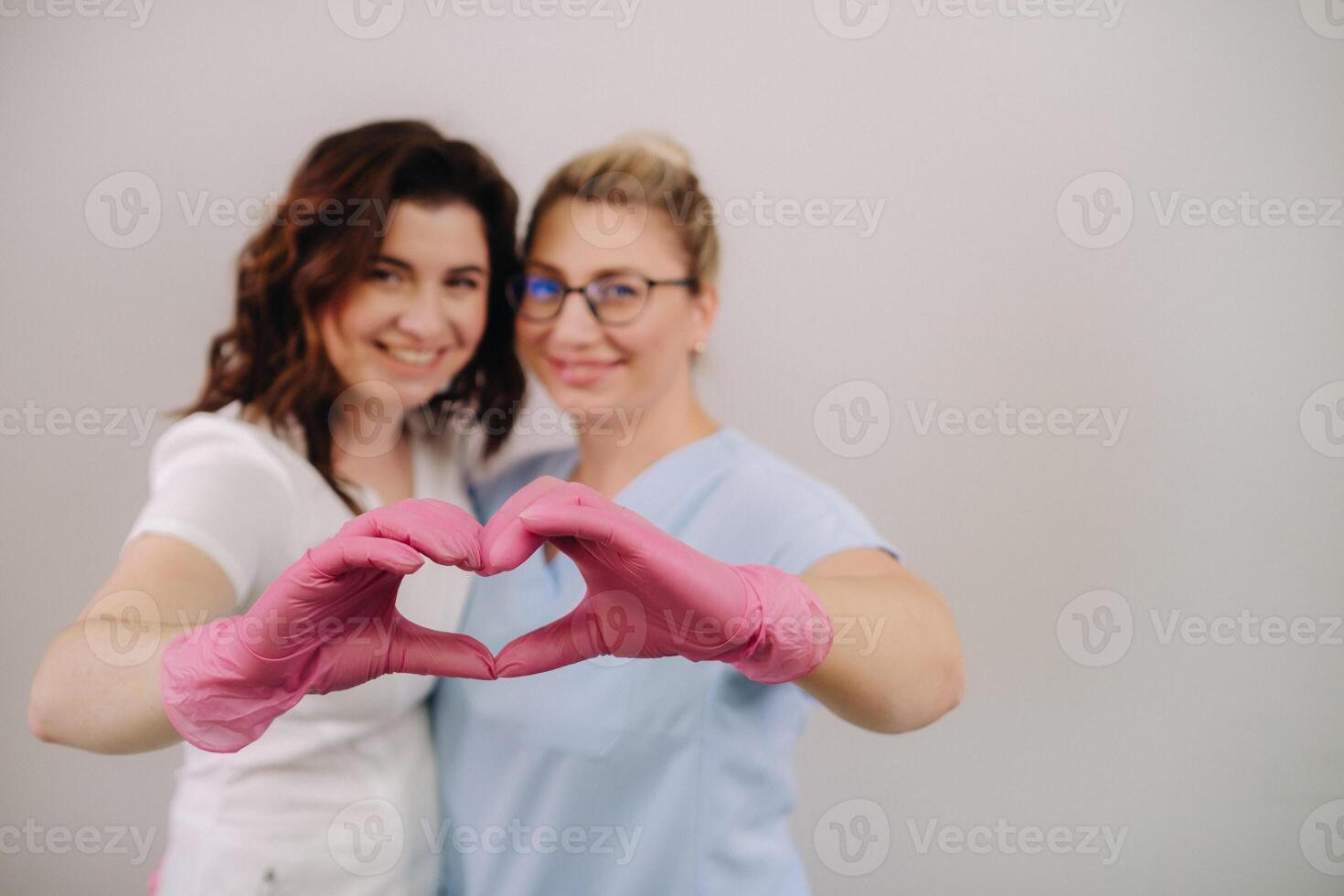 Portrait of two qualified cosmetologists-women, confidently smiling and making a heart with their hands in a medical center photo