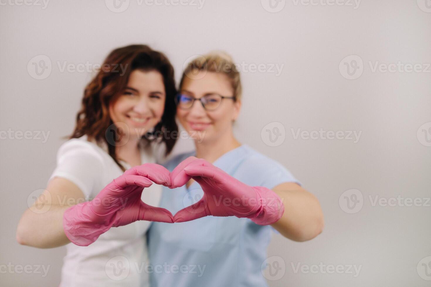 Portrait of two qualified cosmetologists-women, confidently smiling and making a heart with their hands in a medical center photo