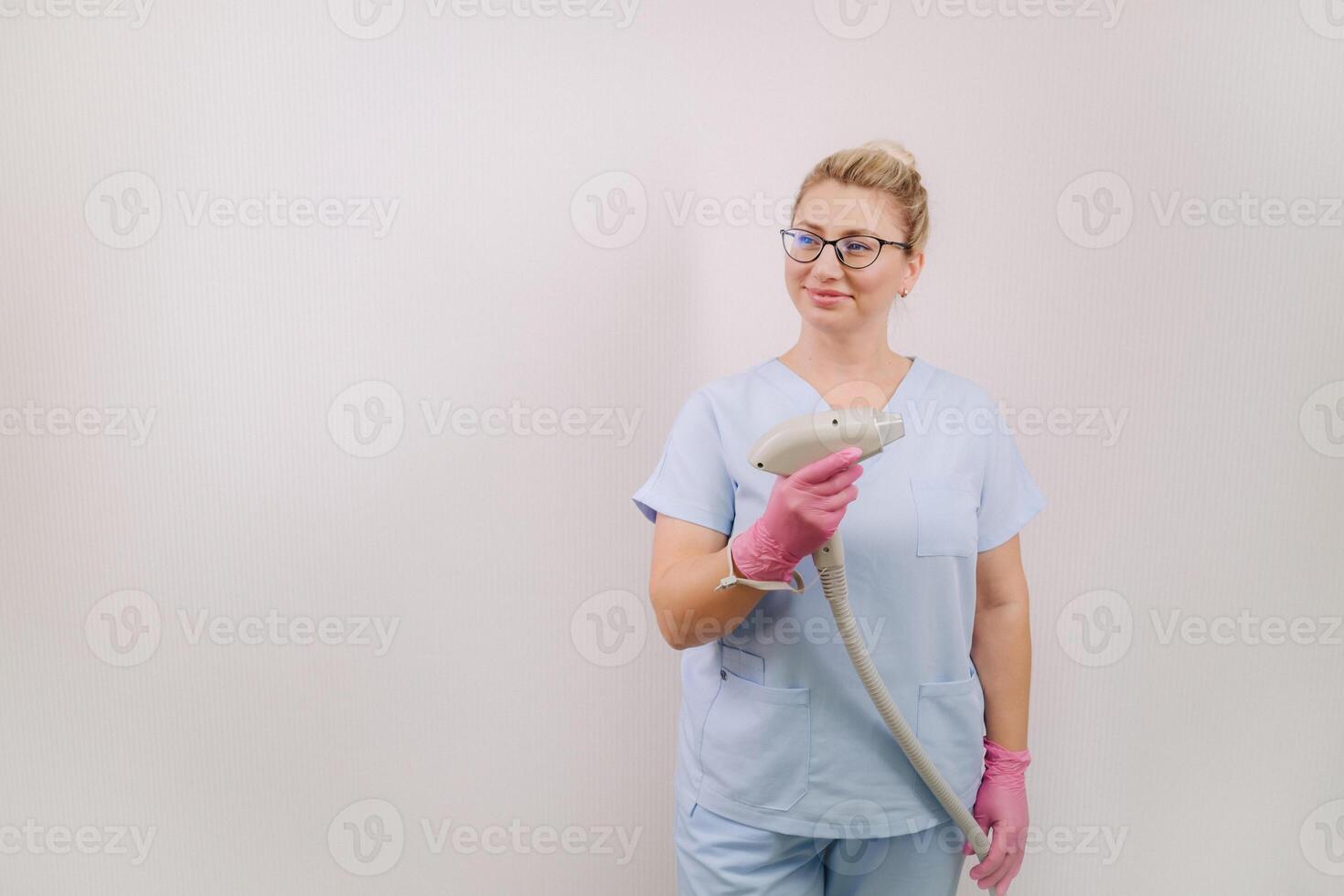 Portrait of the master of laser hair removal. A woman in a blue robe holds a laser hair removal device in her hands photo