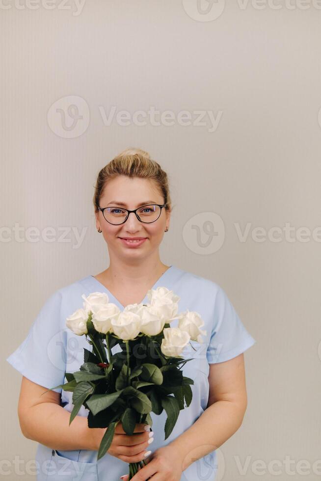 A female doctor in a blue robe with a bouquet of white roses in her hands photo