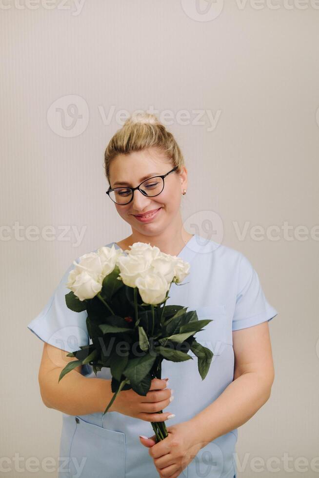 A female doctor in a blue robe with a bouquet of white roses in her hands photo