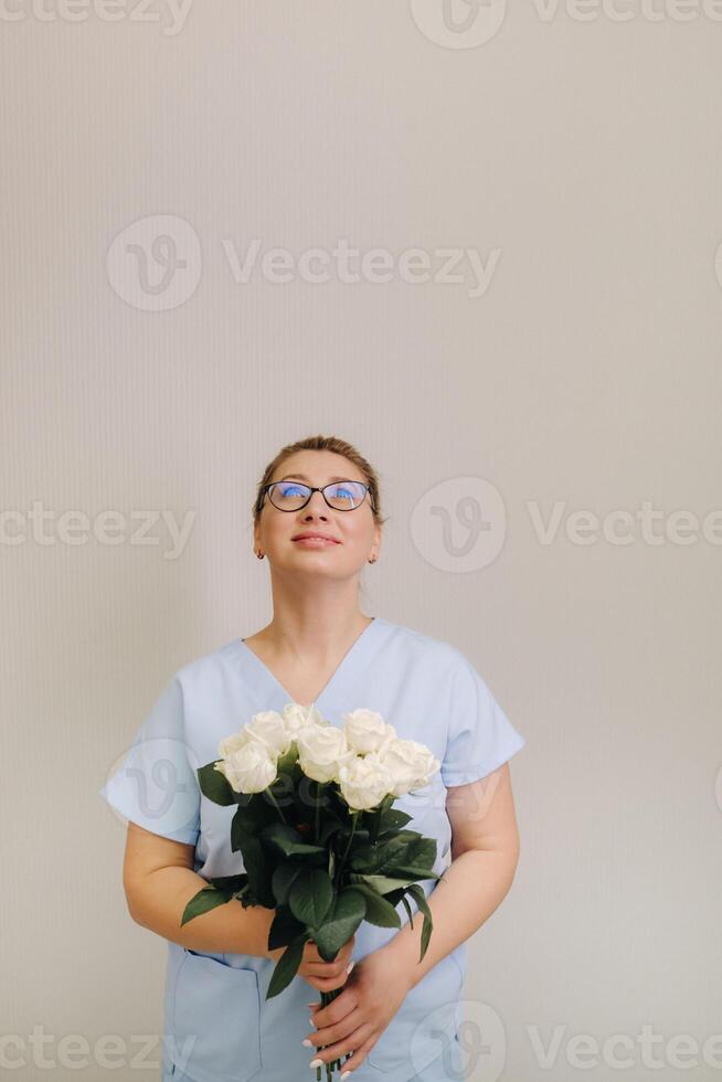 A female doctor in a blue robe with a bouquet of white roses in her hands photo