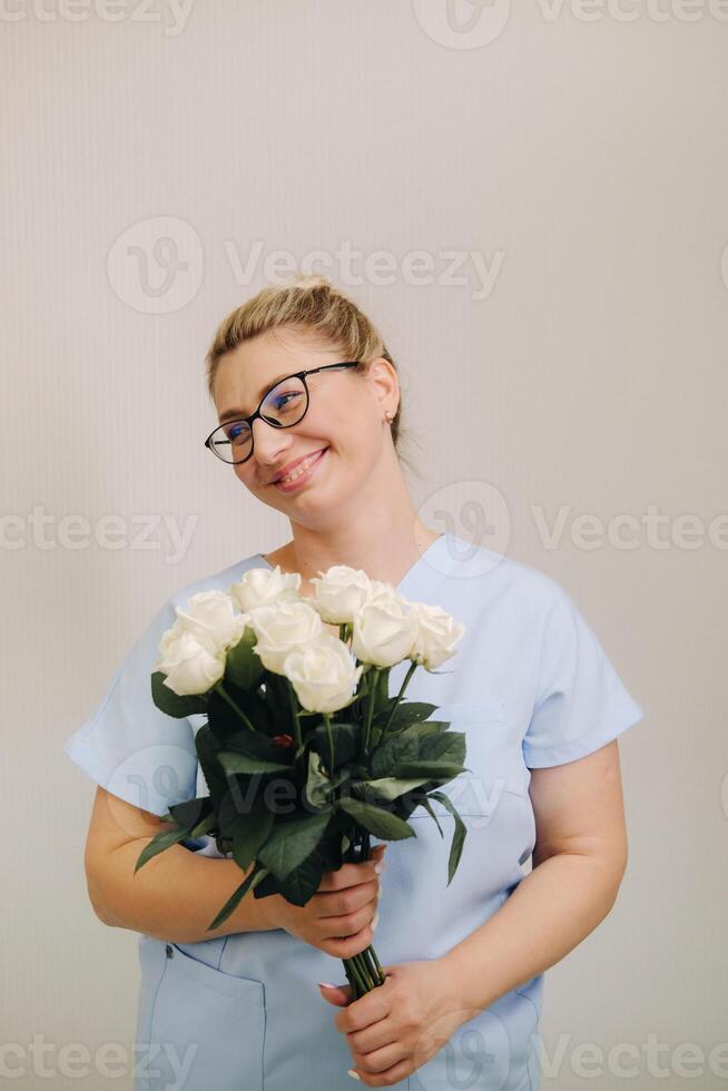 A female doctor in a blue robe with a bouquet of white roses in her hands photo