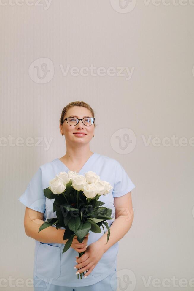 A female doctor in a blue robe with a bouquet of white roses in her hands photo
